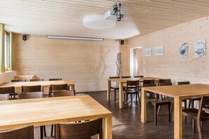 Una habitación amplia con paredes y techo de madera, que incluye varias mesas y sillas de madera, un proyector y obras de arte colgadas en la pared.