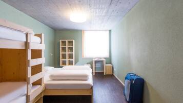Une chambre avec un lit superposé, un petit bureau, une fenêtre et une valise.
