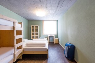 Una habitación con literas, un escritorio pequeño, una ventana y una maleta.