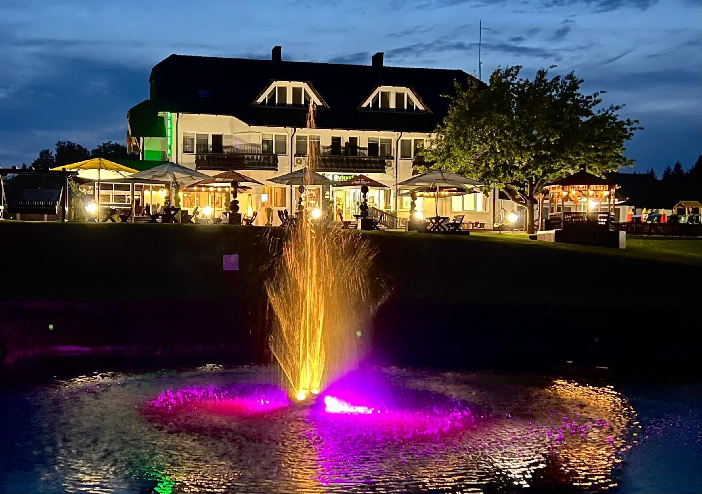 A building with a large fountain in front, surrounded by outdoor seating areas and a tree.