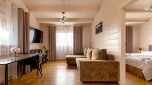 Une pièce avec un plancher en bois, un canapé, un bureau avec une chaise, un lit et un téléviseur fixé au mur.