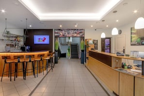 A bar area with stools, a TV screen, and a staircase leading to a bar area. - Butenas Hotel Tyla (Biržai)