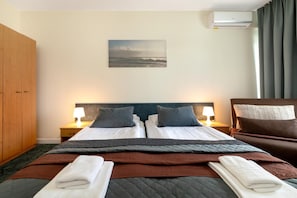A hotel room with a bed, two bedside tables with lamps, a painting on the wall, and an air conditioning unit. - Butenas Hotel Tyla (Biržai)