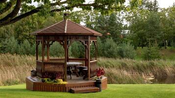 A wooden gazebo with a roof, surrounded by a grassy area, near a body of water.