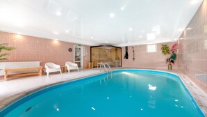 Une piscine à l’eau d’un bleu limpide, entourée d’un mur carrelé, d’un banc et de deux chaises blanches.