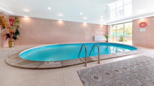 Une piscine intérieure d’une profondeur de 1,35 mètre, entourée de murs recouverts de carreaux beiges et agrémentée d’un tapis à motifs.