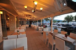 An outdoor cafe with tables and chairs, a covered seating area, and a view of the street. - El Greco (Igoumenitsa)