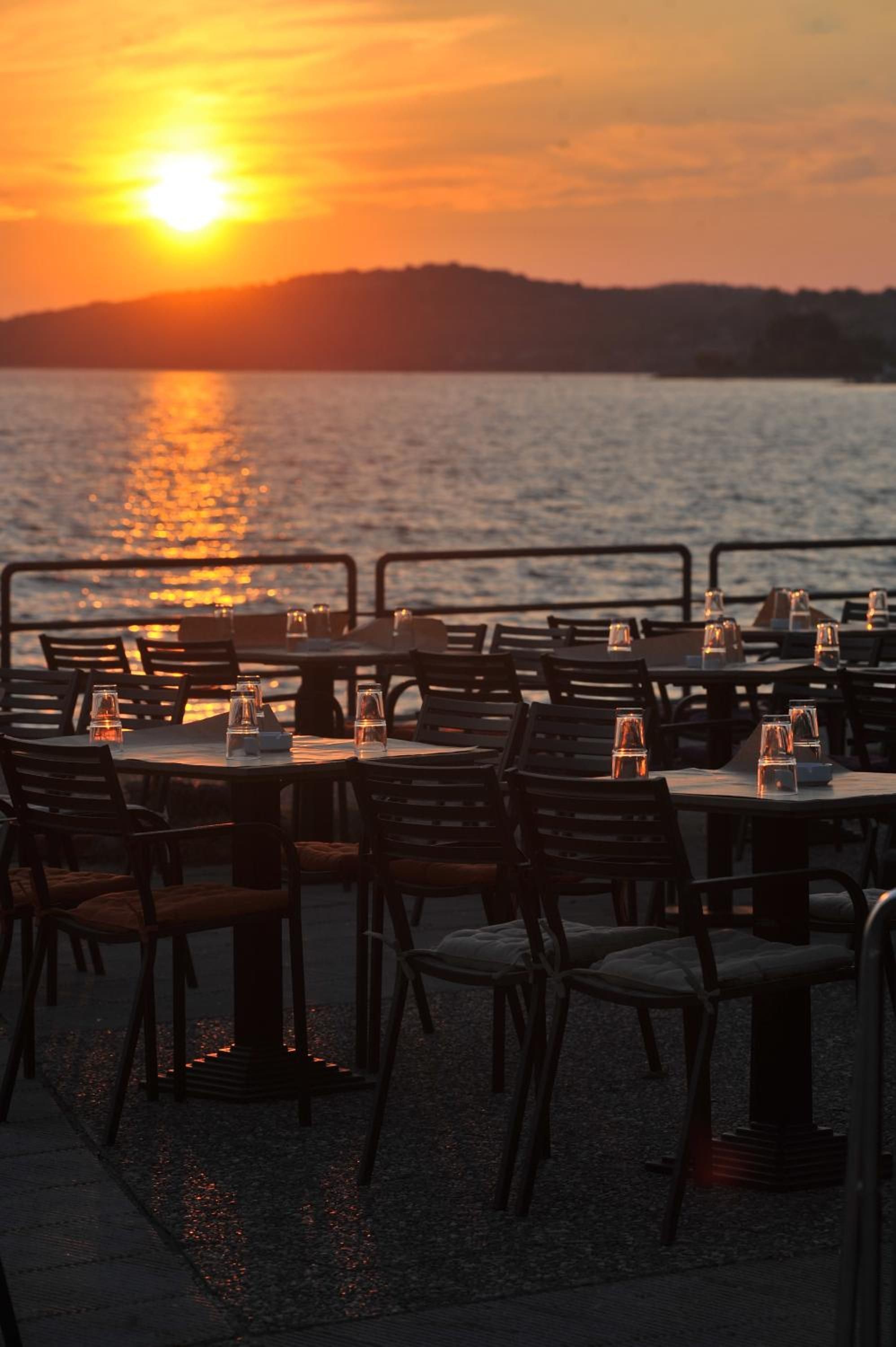 Un espace extérieur aménagé pour les repas, avec des tables et des chaises, offrant une vue sur un plan d’eau au coucher du soleil.
