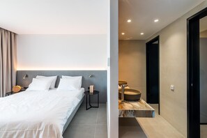 A modern hotel room with a bed, bedside tables, and a bathroom with a sink and mirror. - El Greco (Igoumenitsa)