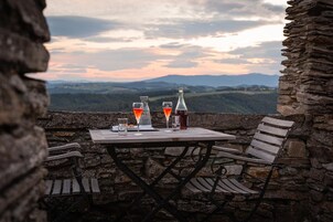 Una mesa con dos vasos y una botella, frente a una vista panorámica de colinas y cielo nublado.