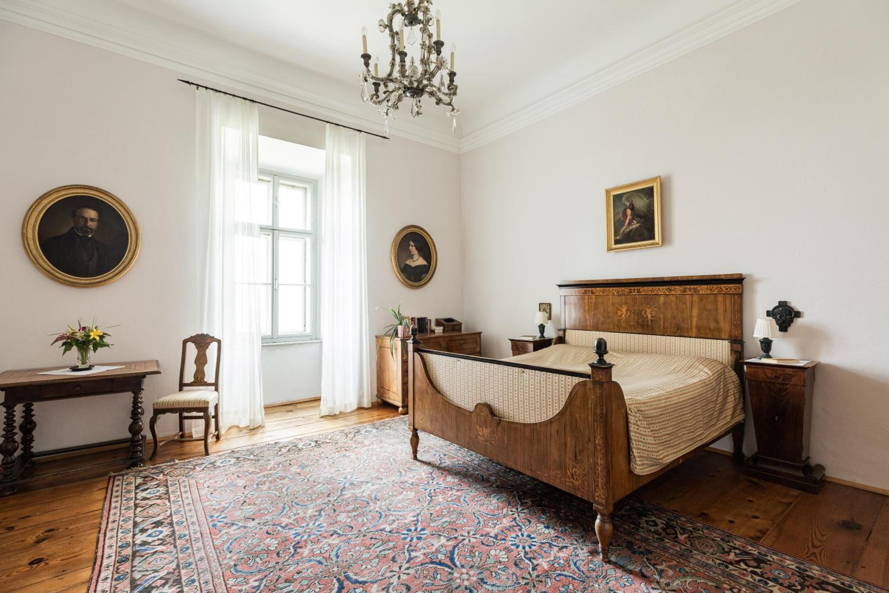 Un dormitorio tradicional con cama de madera, un ventanal grande y una araña.