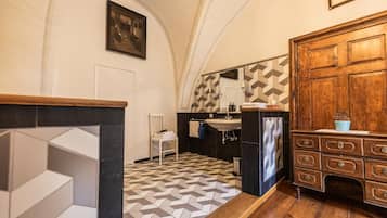 Ein Badezimmer mit einem geometrisch gemusterten Boden, einem Holzschrank mit Schubladen, einem weißen Stuhl und einem Spiegel über dem Waschbecken.