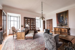 A spacious room with a large bookcase, a sofa, a desk, and a chess table.