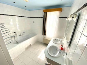 A modern bathroom with a bathtub, two sinks, and a large mirror.