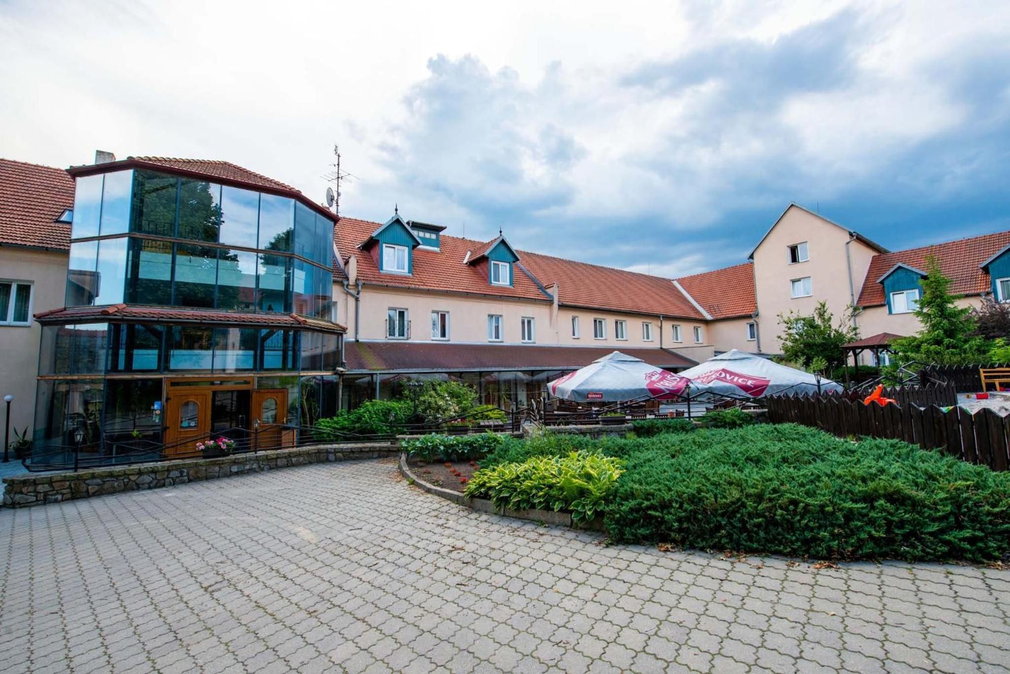 Ein Innenhof mit einem Glasgebäude, einer Holzkonstruktion und einer gepflasterten Fläche mit Bepflanzung.