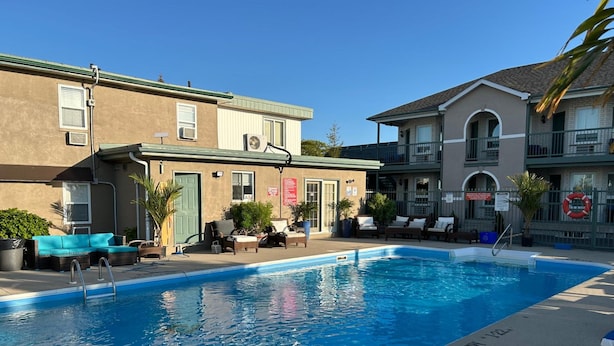 Une piscine dotée de chaises longues et d’une bouée de sauvetage, entourée de bâtiments avec des espaces de détente en plein air et des plantes.