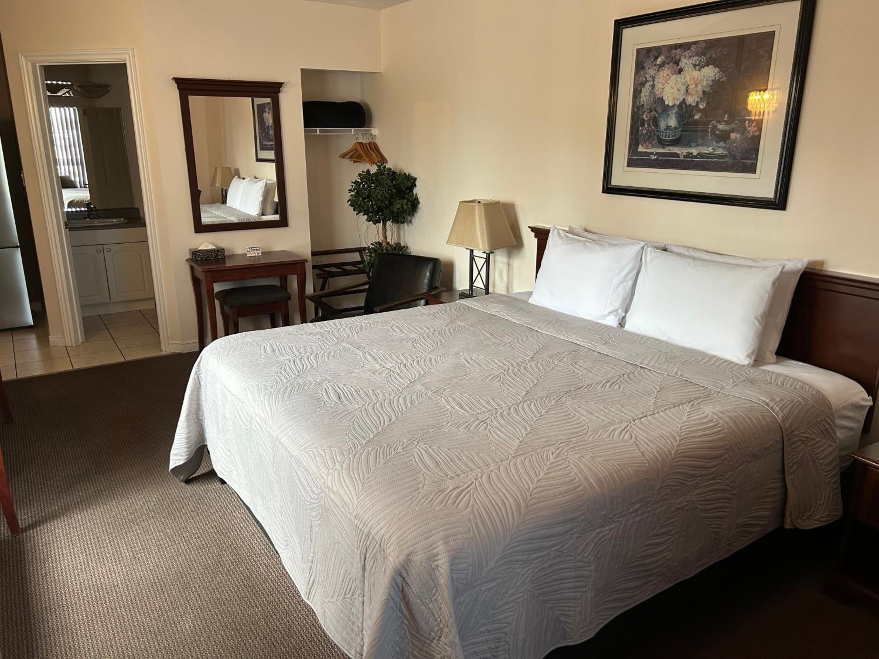 A hotel room with a large bed, a desk, a chair, a lamp, a mirror, and a framed picture on the wall.