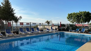 Une piscine équipée de chaises longues et d’un panneau indiquant une zone peu profonde et interdisant la plongée.