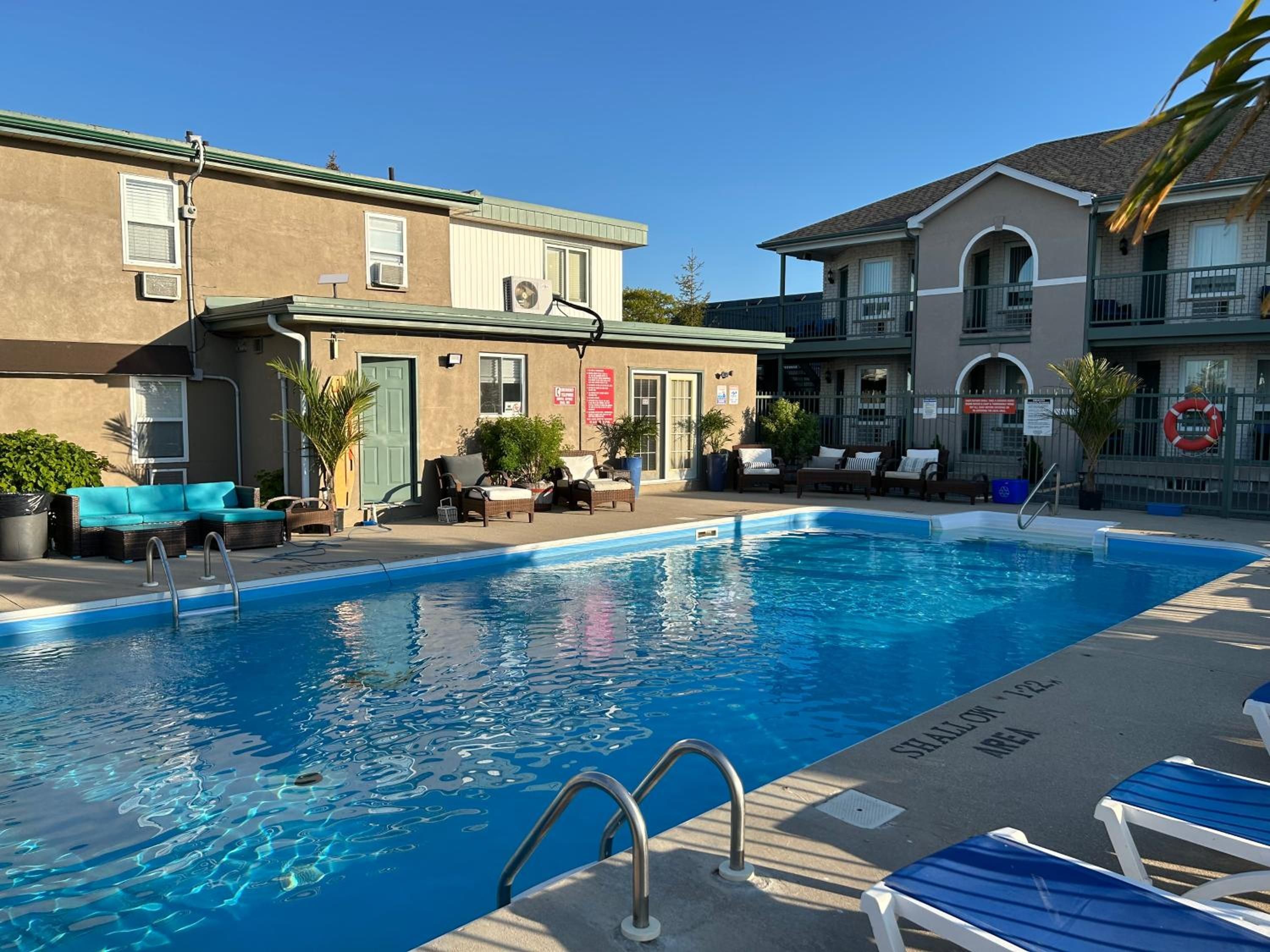 A swimming pool with lounge chairs and a lifebuoy, surrounded by buildings with outdoor seating and plants.