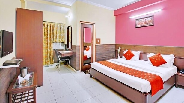 A hotel room with a bed, bedside table, and a desk with a chair. - Hotel Mantri Residency (Ranchi)
