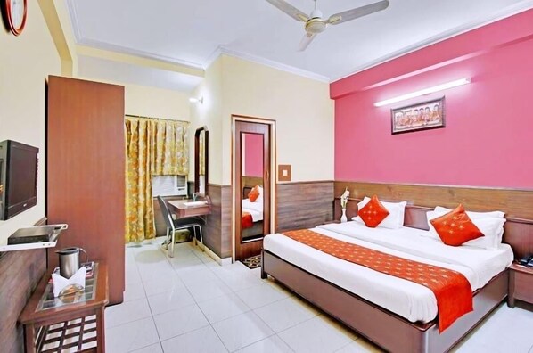 A hotel room with a bed, bedside table, and a desk with a chair. - Hotel Mantri Residency (Ranchi)