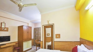 A hotel room with a bed, a desk, a chair, a wardrobe, a ceiling fan, and a bathroom door. - Hotel Mantri Residency (Ranchi)
