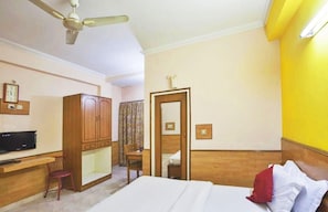 A hotel room with a bed, a desk, a chair, a wardrobe, a ceiling fan, and a bathroom door. - Hotel Mantri Residency (Ranchi)