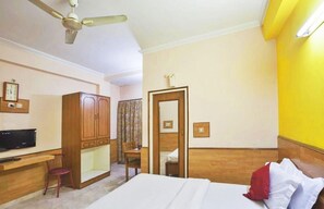Een hotelkamer met een bed, een bureau, een stoel, een kledingkast, een plafondventilator en een badkamers deur.