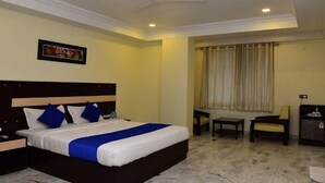 A hotel room with a bed, a desk, a chair, and a small cabinet. - Hotel Mantri Residency (Ranchi)