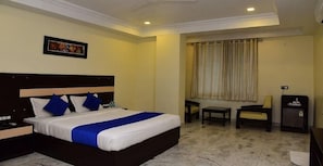 A hotel room with a bed, a desk, a chair, and a small cabinet. - Hotel Mantri Residency (Ranchi)