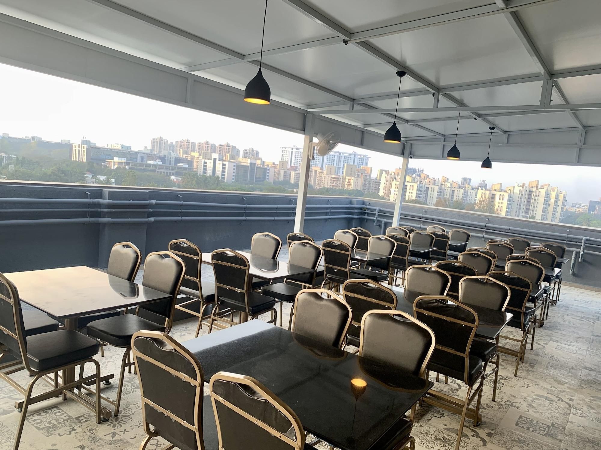 Eine Dachterrasse mit Tischen und Stühlen, Blick auf die Stadt und hängenden Pendelleuchten.