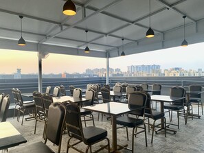 A rooftop restaurant with tables and chairs, city skyline views, and hanging pendant lights. - Staybird - Fortune House Business Hotel (Pune)