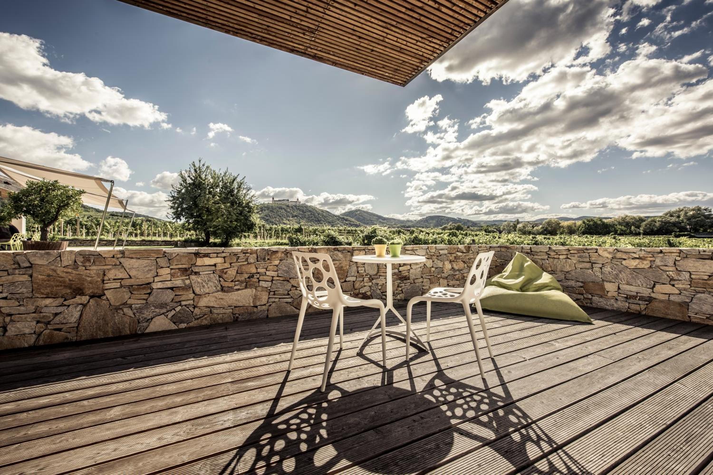 Eine Terrasse im Freien mit einer Steinwand, zwei Stühlen, einem Tisch und einem Holzboden.