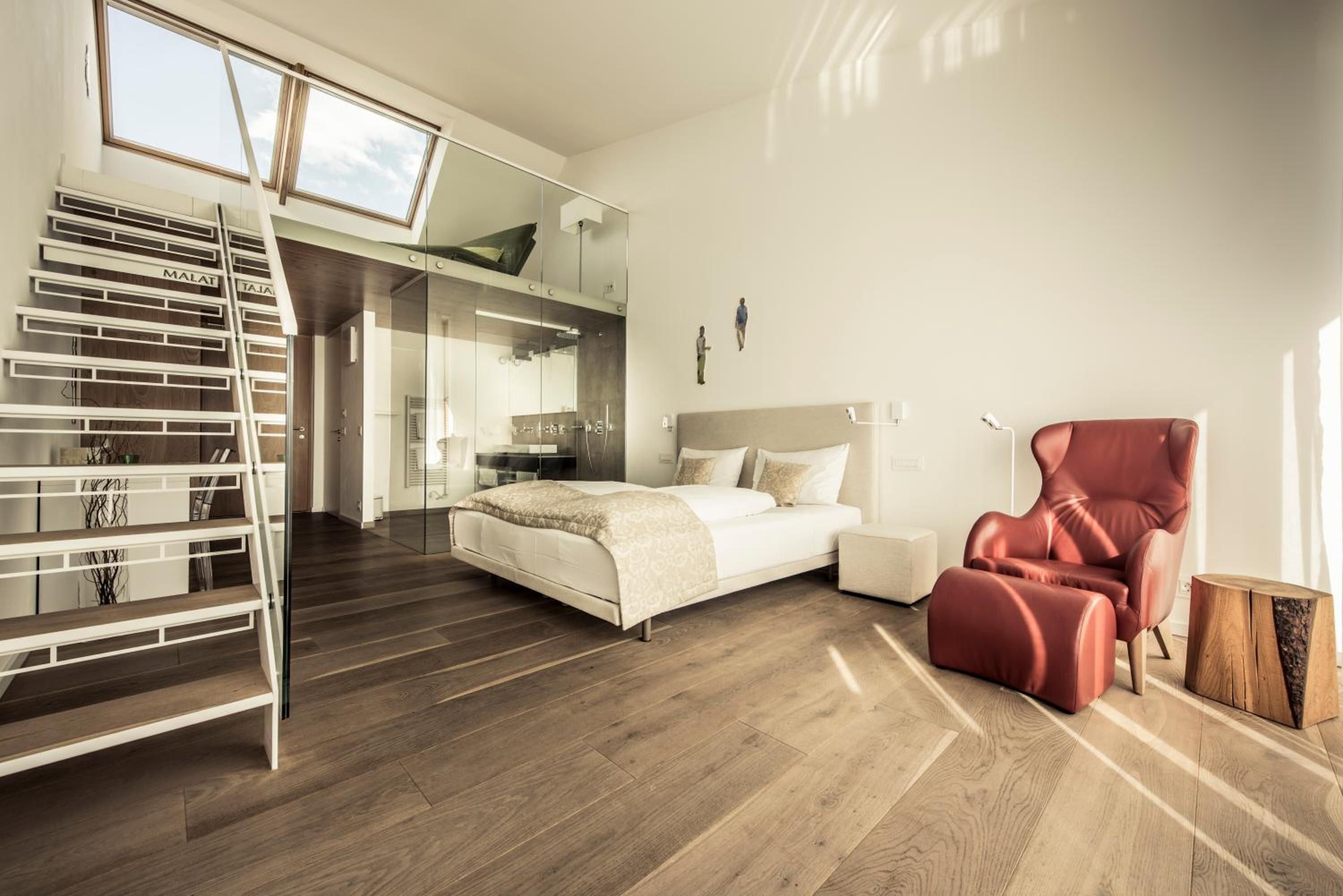 Ein modernes Schlafzimmer mit einer Erkerliege, einem Bett, einem roten Sessel und Holzboden.