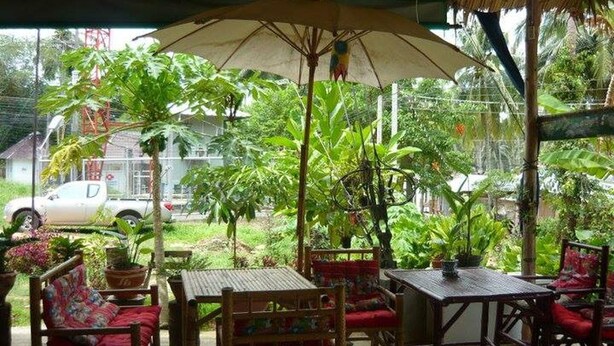 An outdoor seating area with tables and chairs, surrounded by lush greenery and a thatched roof structure. - Day Night Bungalow Bar (Ko Chang)