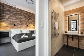 A modern bedroom with a brick-patterned wall, a bed with white linens, and a bedside table. - Vaci Boutique Loft Suites By Bqa (Budapest)