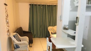 Habitació petita amb una cadira blanca, un sofà marró, una cortina verda i una taula blanca.