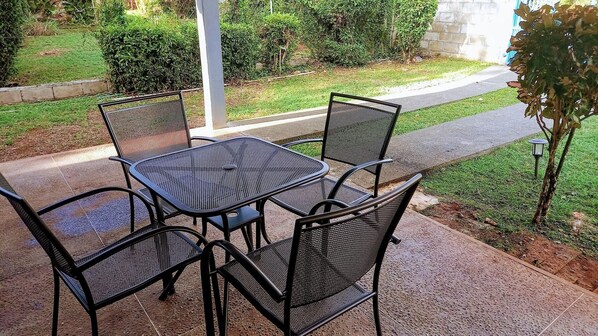 Un patio al aire libre con una mesa y sillas de metal, rodeado de un jardín y un sendero.
