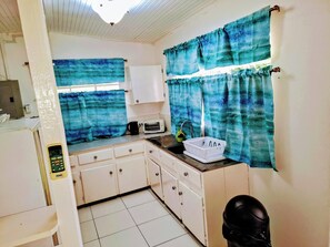 Una cocina compacta con armarios blancos, una pequeña encimera y un ventanal con cortinas azules.