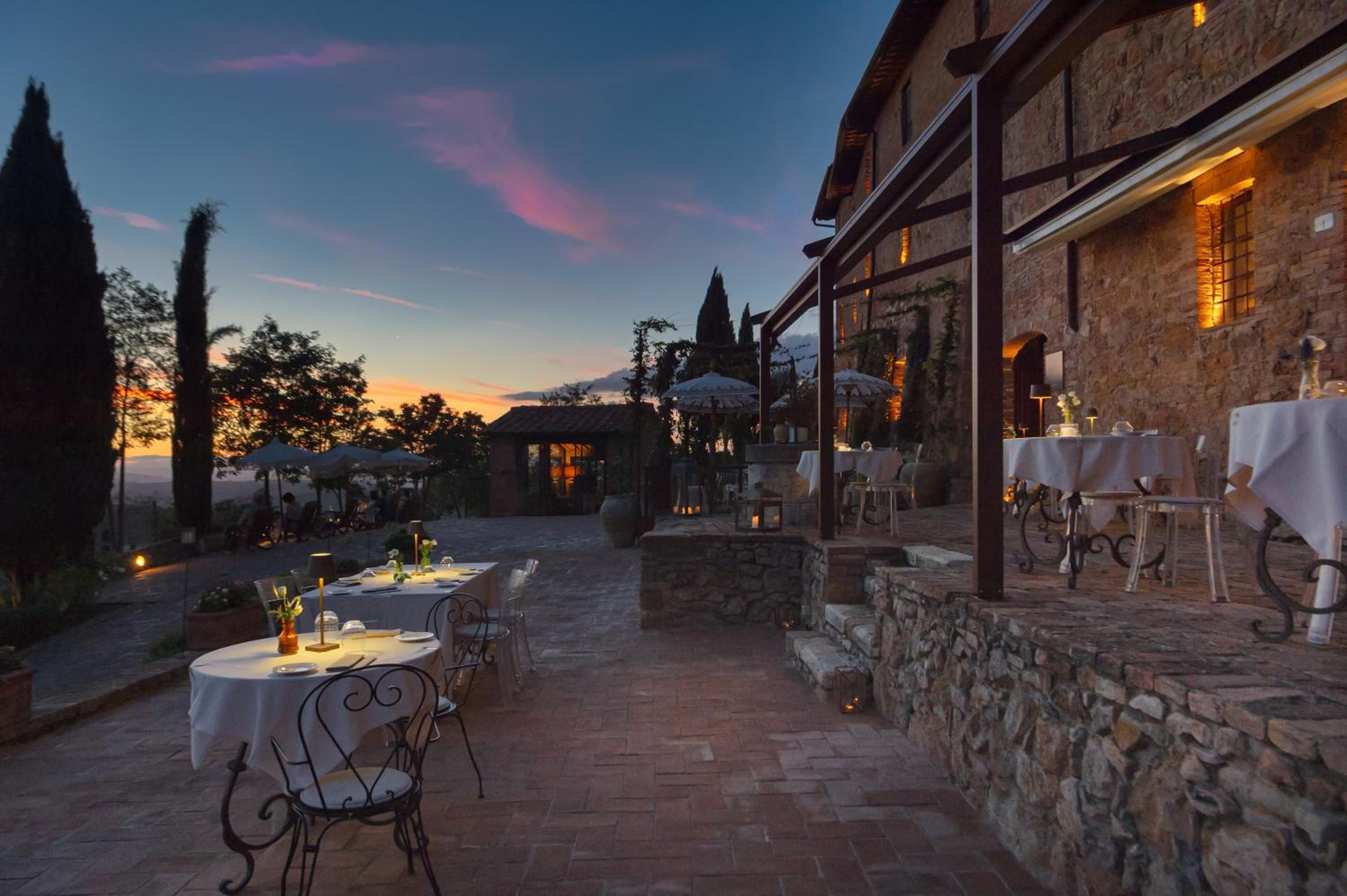An outdoor dining area with stone walls, tables set for two, and umbrellas.