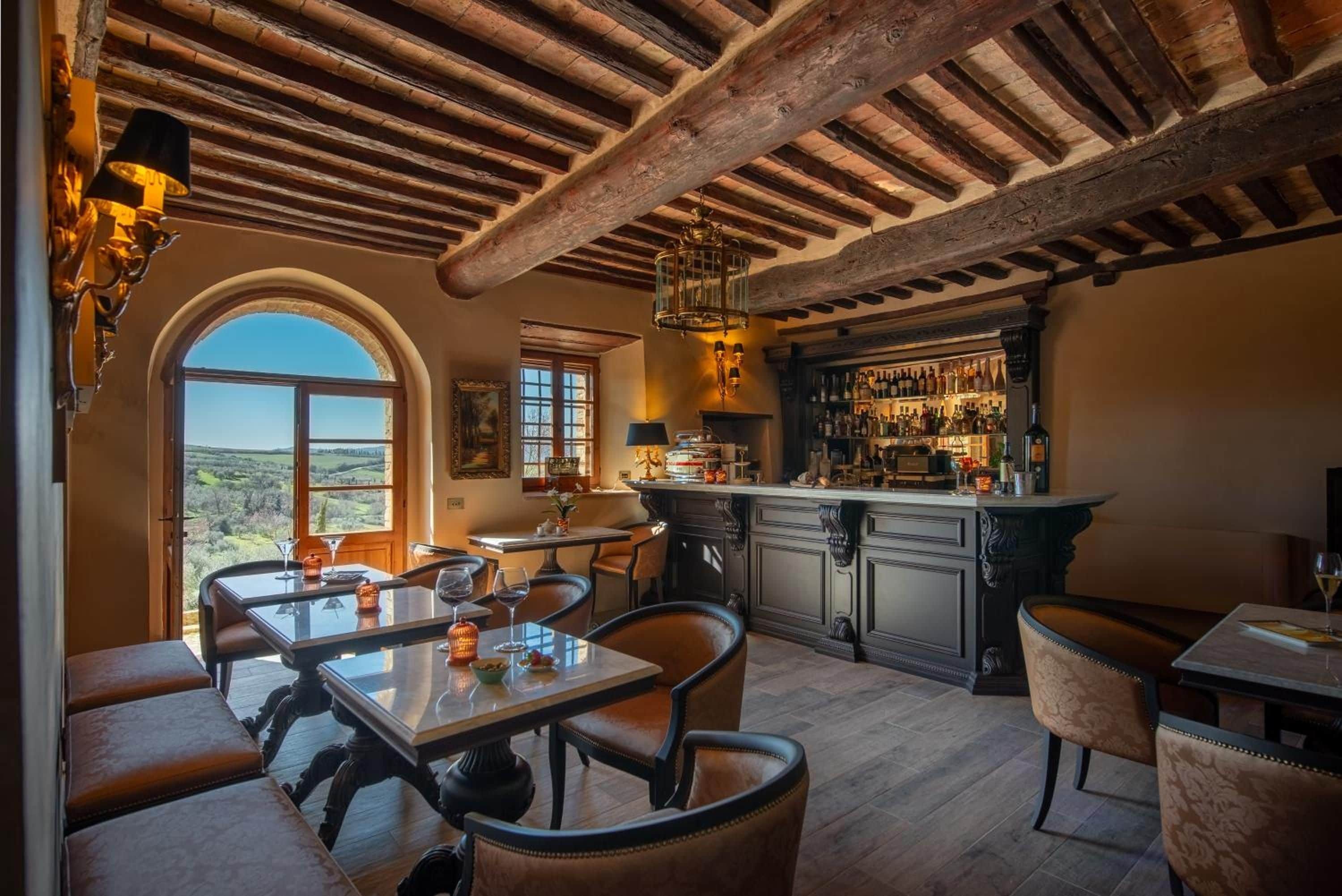 Zona pranzo con vista sulla campagna, un bar con assortimento di bottiglie e un soffitto in legno rustico.