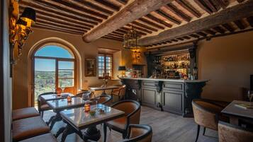 Zona pranzo con vista sulla campagna, un bar con assortimento di bottiglie e un soffitto in legno rustico.