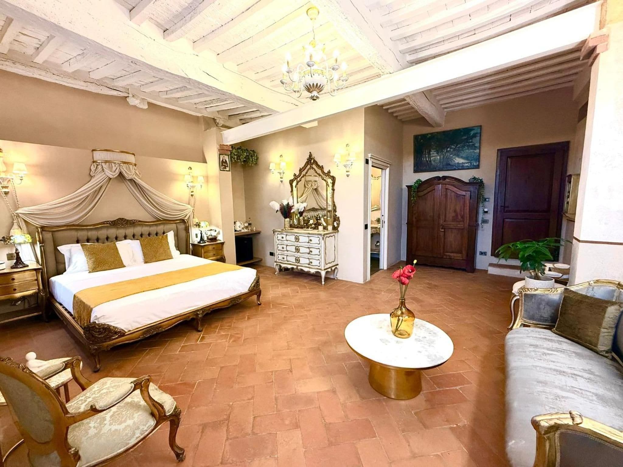Un'ampia stanza con un letto grande, un lampadario classico, una cassettiera bianca e un divano.