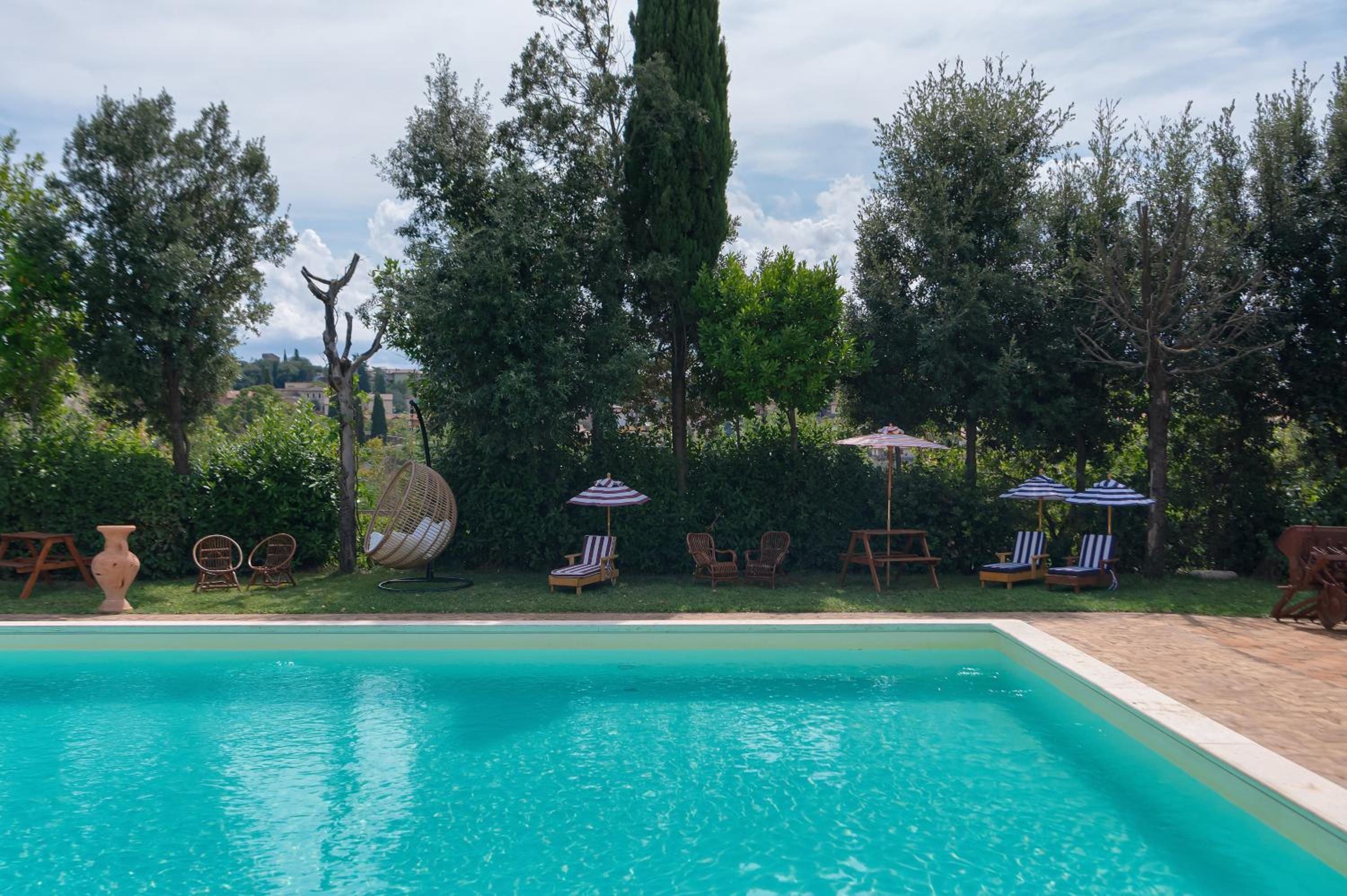 A swimming pool with lounge chairs and umbrellas, surrounded by trees and greenery.
