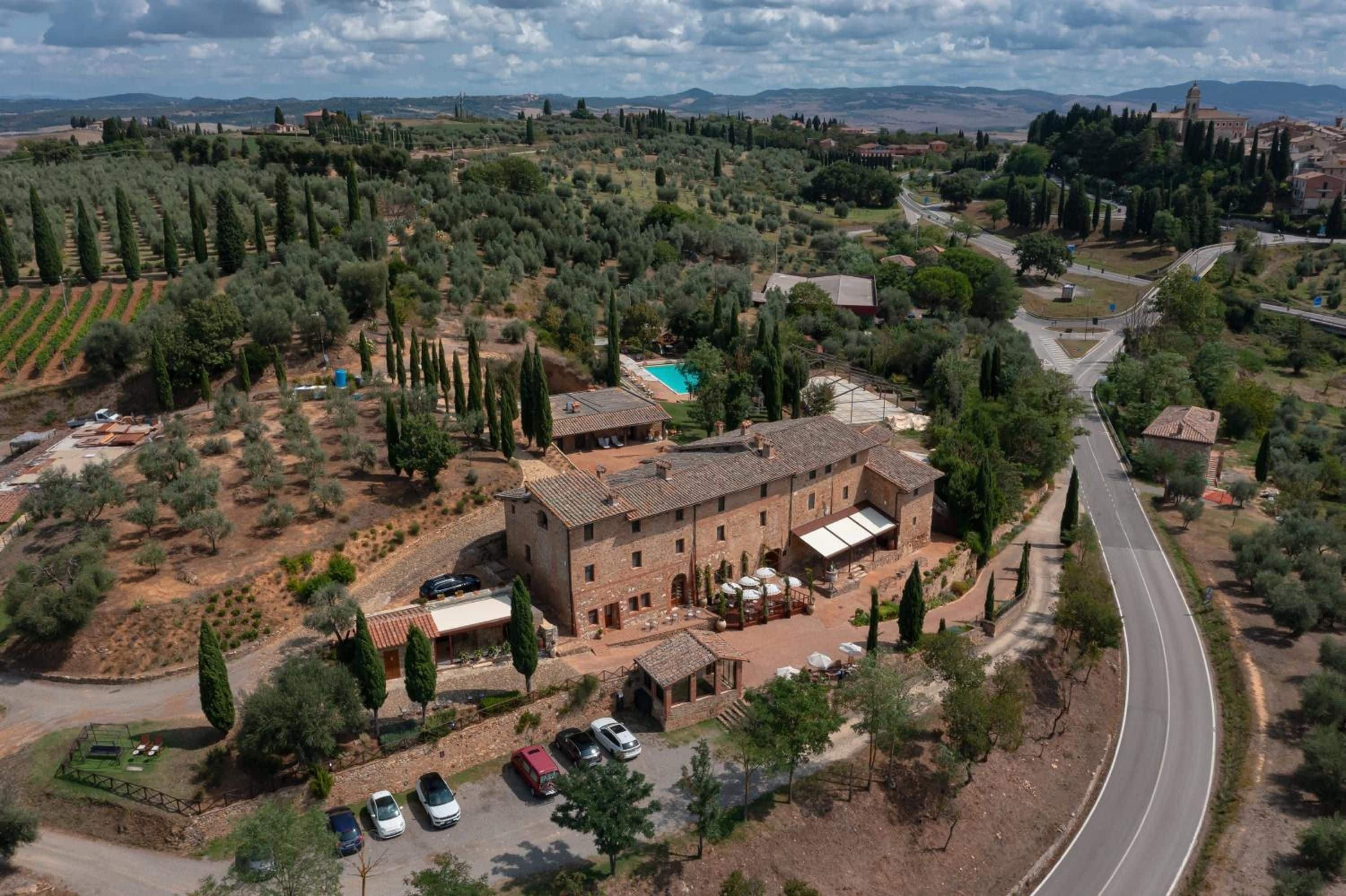 Un grande edificio con un cortile, circondato da uliveti e una strada tortuosa.