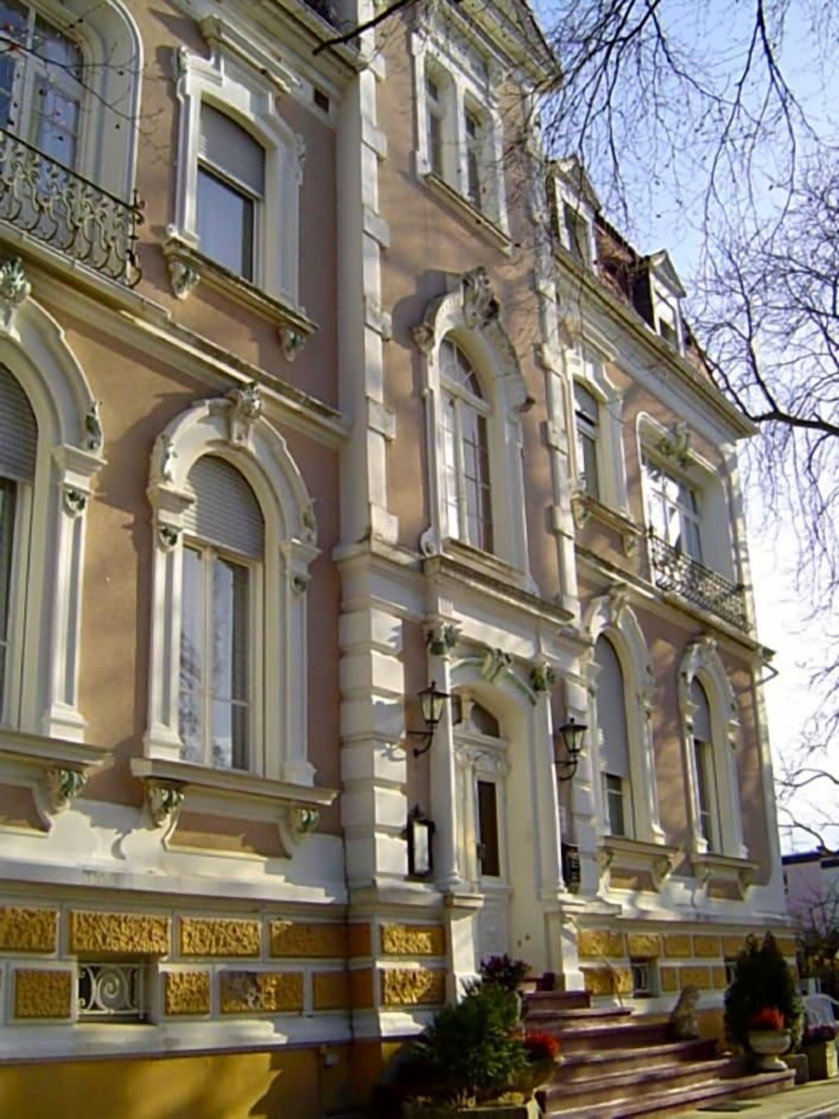 Un edificio de varios pisos con detalles arquitectónicos ornamentales, incluyendo ventanas en arco y molduras decorativas.