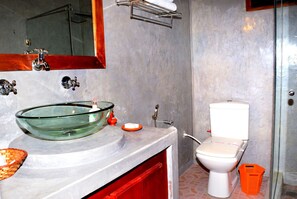 Un baño con lavamanos de vidrio, inodoro y zona de ducha.