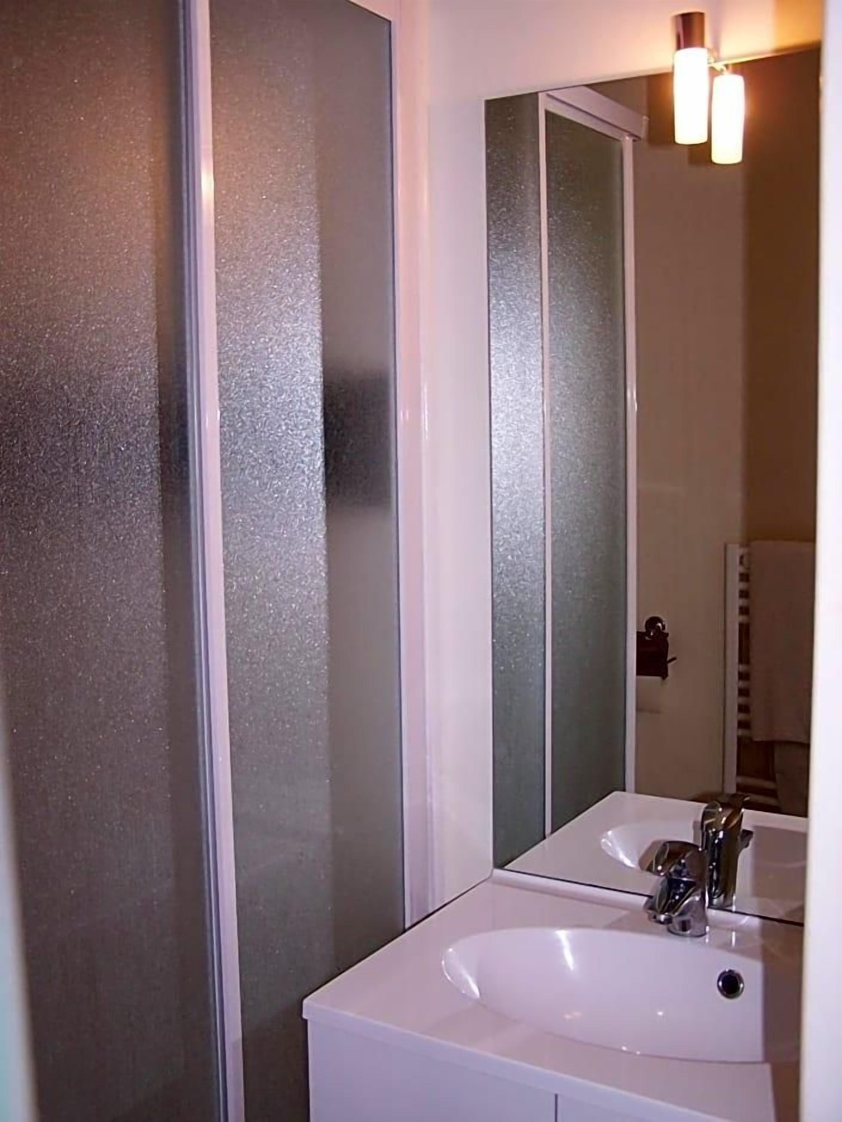 A bathroom with a white sink, a mirror, and frosted glass doors.