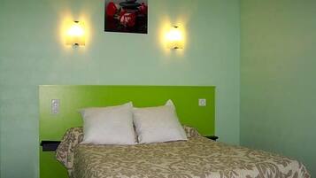 A room with a green wall, a bed with a patterned bedspread, two wall-mounted lights, and a framed picture above the bed.