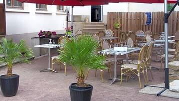 An outdoor patio with tables and chairs, potted plants, and red umbrellas.